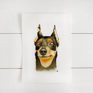 May include: Watercolor painting of a black and tan dog with brown eyes. The dog is looking directly at the viewer with a slight smile.