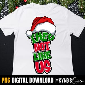 May include: White t-shirt with a Christmas-themed graphic. The design features a red and white Santa hat above the text "THEY NOT LIKE US" in green and red. The bottom of the shirt has the text "PNG DIGITAL DOWNLOAD".