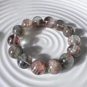 Op de afbeelding: Een armband gemaakt van ronde, heldere, iriserende kralen met hints van groen, bruin en rood. De kralen zijn aan elkaar geregen op een helder elastisch koord.