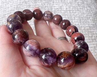 May include: A purple and red amethyst gemstone bracelet with round beads. The bracelet is made of natural stones and has a unique, swirling pattern.