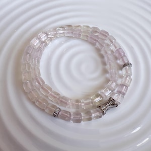 May include: A double-wrap bracelet made of pale pink and clear glass beads with a silver bow charm.