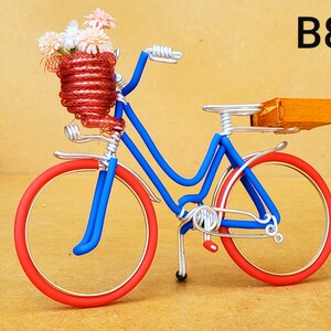 May include: A miniature bicycle sculpture with a blue frame, red wheels, and a red basket filled with flowers. The bicycle has a small wooden box on the back. The text "B8" is in the upper right corner.