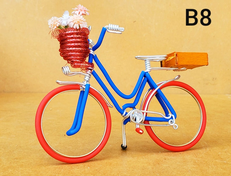 May include: A miniature bicycle sculpture with a blue frame, red wheels, and a red basket filled with flowers. The bicycle has a small wooden box on the back. The text "B8" is in the upper right corner.
