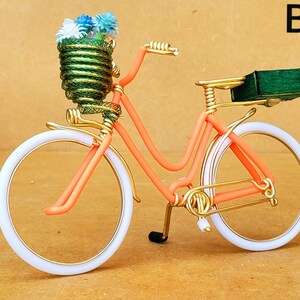 May include: A decorative bicycle sculpture with an orange frame, white tires, and gold accents. The front basket is filled with blue and white flowers. A small green box is on the back. The text "B9" is in the upper right corner.