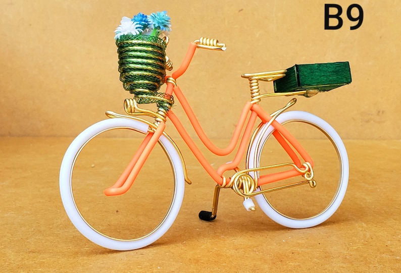 May include: A decorative bicycle sculpture with an orange frame, white tires, and gold accents. The front basket is filled with blue and white flowers. A small green box is on the back. The text "B9" is in the upper right corner.