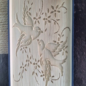 Könnte beinhalten: Ein Buch mit einem dekorativen Design aus zwei Vögeln und floralen Ranken, die aus den Seiten geschnitten sind. Das Buch ist in blauen Stoff gebunden.