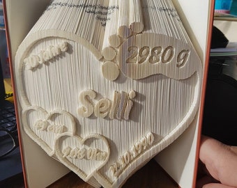 May include: A white book folded into the shape of a heart with the name "Selin" and the date "20.06.1990" inside. The heart is surrounded by two smaller hearts with the text "2980g" and "30.06.1990".