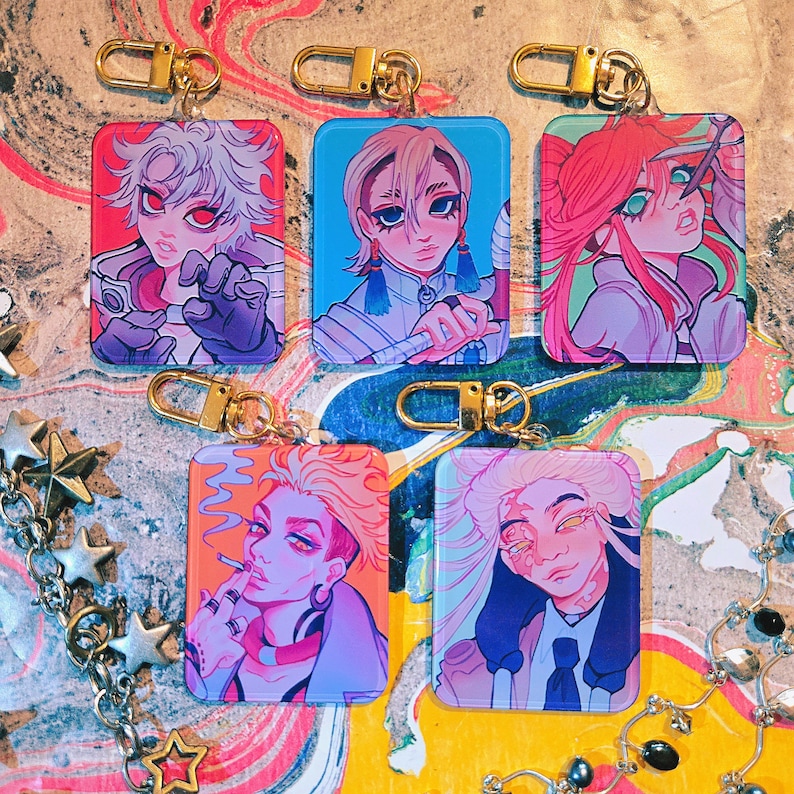 Puede incluir: Una colecci&oacute;n de llaveros rectangulares con retratos coloridos de estilo anime y cierres dorados. Cada llavero muestra un personaje diferente con peinados y expresiones &uacute;nicas, sobre fondos vibrantes.