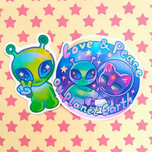 May include: Two stickers featuring a green alien and a cat in a spacesuit. The alien sticker says "Love & Peace on Planet Earth".