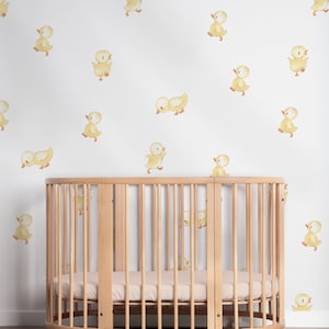 May include: A white wall with a yellow duckling pattern, featuring a wooden oval crib with a beige mattress.