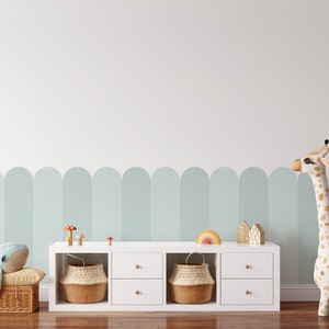 May include: A white shelf unit with four drawers and two woven baskets. The shelf is against a white wall with a light blue and white arched pattern. A stuffed giraffe and whale are on the floor in front of the shelf.