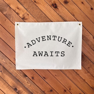 May include: White canvas wall flag with black text that reads ".ADVENTURE. AWAITS."