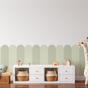 Pode incluir: Estante branca com duas gavetas e duas prateleiras abertas. As prateleiras s&atilde;o decoradas com cestos de vime, brinquedos de madeira e um arco-&iacute;ris. Uma girafa de pel&uacute;cia fica do lado direito da estante. A parede atr&aacute;s da estante &eacute; pintada de verde claro com uma fileira de arcos verdes.