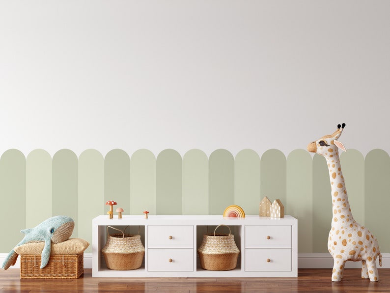Pode incluir: Estante branca com duas gavetas e duas prateleiras abertas. As prateleiras s&atilde;o decoradas com cestos de vime, brinquedos de madeira e um arco-&iacute;ris. Uma girafa de pel&uacute;cia fica do lado direito da estante. A parede atr&aacute;s da estante &eacute; pintada de verde claro com uma fileira de arcos verdes.