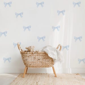 May include: A wicker basket with a white blanket inside, sitting on a light brown rug in front of a white wall with blue watercolor bow decals.