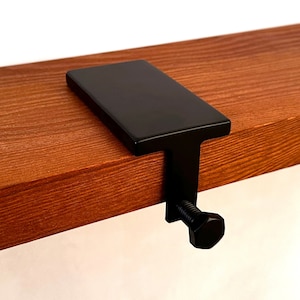 Può includere: Mensola a muro in metallo nero con parte superiore piatta e una vite per il fissaggio a uno scaffale in legno.