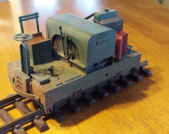May include: A green model train engine with a black steering wheel, two red levers, and a black metal grate. The engine is on a wooden track and has a black fuel tank and a black metal grate on the side.