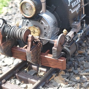 Puede incluir: Primer plano de una locomotora de tren de juguete negra y plateada con una plataforma de madera y un cabrestante de cuerda. La locomotora tiene el número "2" en dorado en el lateral y el texto "H.K. Porter & Co.". El tren está sobre vías.