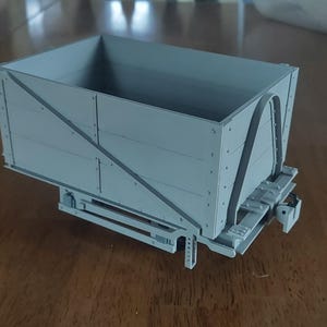 May include: A gray model train car with a rectangular box body and a detailed undercarriage. The car is made of plastic and has a realistic design.