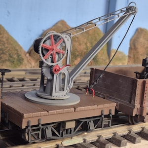 May include: A detailed model of a railway crane, painted in gray, red, and brown. The crane features a large gear and a boom, mounted on a flatbed car. The model includes a second car with a detailed engine. The scene is set on miniature train tracks.