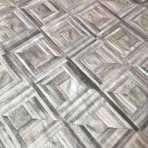 May include: A gray and white patchwork rug with a geometric pattern. The rug is made of leather and has a soft, luxurious feel.