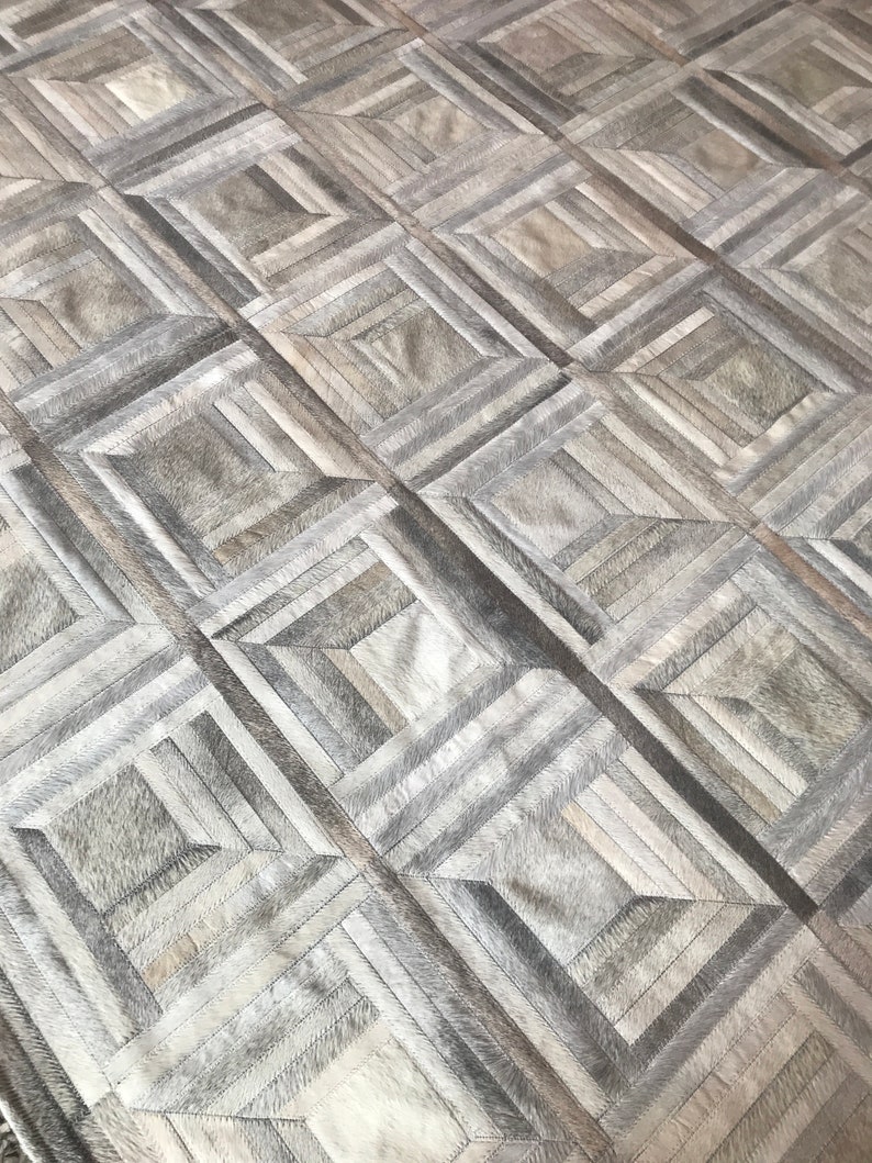 May include: A gray and white patchwork rug with a geometric pattern. The rug is made of leather and has a soft, luxurious feel.