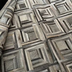 May include: A geometric patterned rug made of various shades of gray and brown leather. The rug is made of small squares and rectangles that are sewn together to create a unique design.