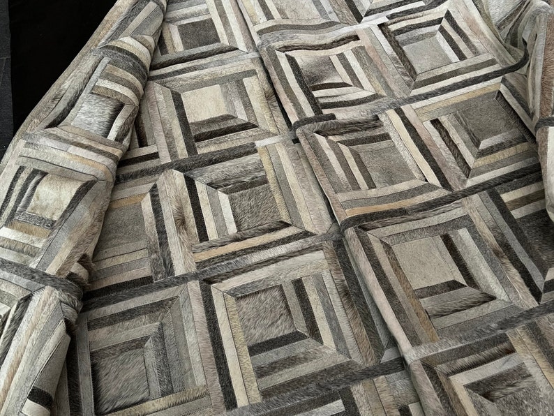 May include: A geometric patterned rug made of various shades of gray and brown leather. The rug is made of small squares and rectangles that are sewn together to create a unique design.