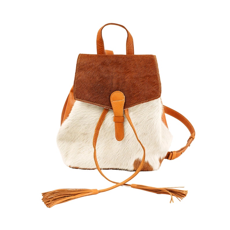 May include: A brown and white cowhide leather backpack with a brown leather flap and tassel accents.