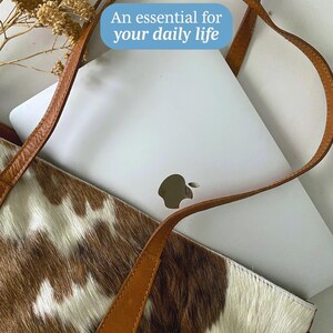 May include: A brown leather tote bag with a cowhide pattern. The bag has a white laptop inside and the text "An essential for your daily life" is superimposed on the image.