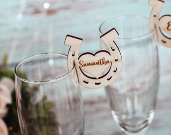 May include: Two wooden horseshoe shaped wedding place card holders with a heart cutout. The place cards are personalised with the names "Samantha" and "Eric".