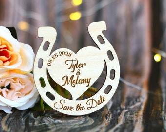 May include: Wooden horseshoe save the date announcement with a heart cutout. The date 03.25.2023, the names Tyler & Melany, and the text "Save the Date" are engraved on the horseshoe.