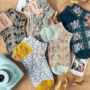 May include: Assortment of six ankle socks with various patterns. The socks are made of a soft, textured fabric and feature intricate designs in shades of green, blue, and beige.