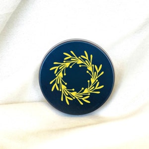May include: A round, dark blue container with a yellow floral wreath design.