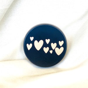 May include: A black round container with a design of white hearts on the front.