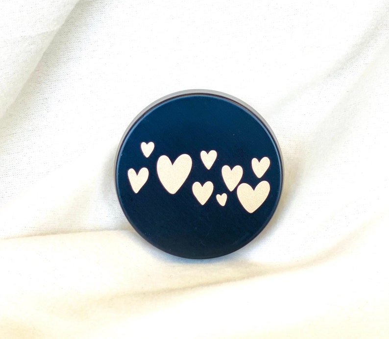 May include: A black round container with a design of white hearts on the front.