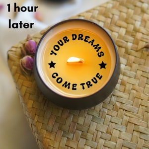 May include: A black candle with a yellow wax top and a white flame. The candle has the text "YOUR DREAMS COME TRUE" printed on the side.