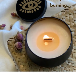 May include: A black candle with a gold eye design on the lid. The candle is lit and the wax is melting. The text "keep on burning..." is written on the image.