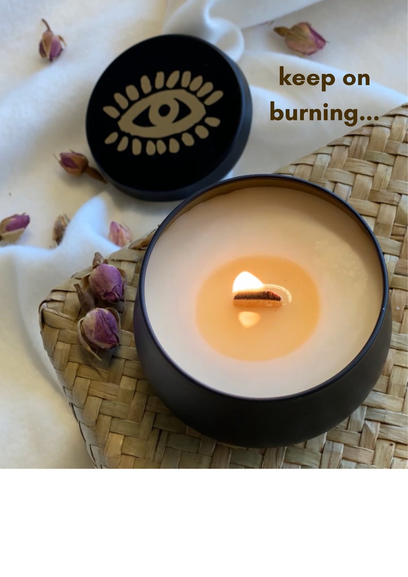 May include: A black candle with a gold eye design on the lid. The candle is lit and the wax is melting. The text "keep on burning..." is written on the image.