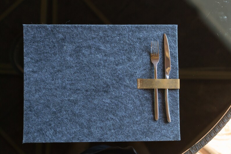May include: A gray felt placemat with a gold metal utensil holder and a fork and knife placed inside.