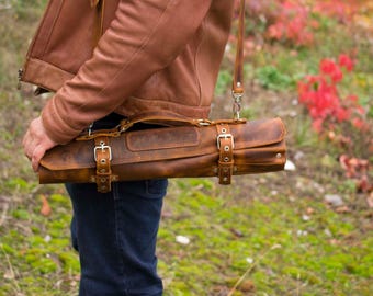 May include: A brown leather knife roll with a strap and buckles. The roll is worn and has a distressed look.