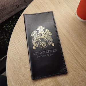 May include: A black leather menu cover with gold embossed lettering that reads "A.T.O. Keeffe's Provisions & Pub" and a gold crest.
