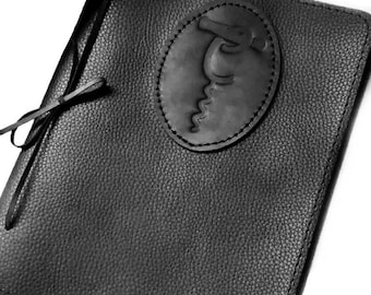 May include: Black leather journal with a stitched oval embossed with a stylized alligator design. The journal has a black leather tie closure.