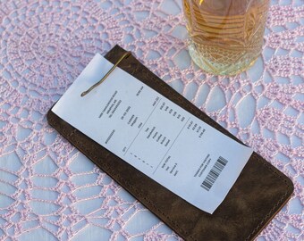 May include: A white receipt with a brown leather folder. The receipt shows a list of items and prices, including "Coffee", "Tea", "Cake", and "Total". The receipt also includes a barcode and the text "Thanks for visiting! Customer Copy".