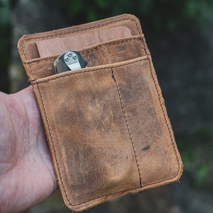 Könnte beinhalten: Eine braune Ledergeldbörse mit mehreren Fächern und einem kleinen Taschenmesser darin.