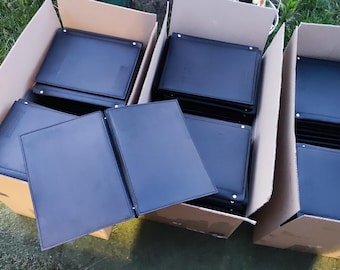 May include: Several black menu covers are stacked inside open cardboard boxes. One menu cover is open, revealing the interior. The boxes are sitting on a grassy surface.