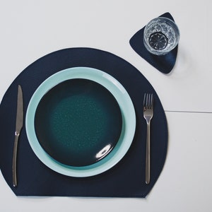 May include: A blue leather placemat with a teal and light blue ceramic plate, a silver fork and knife, and a glass of water on a triangular coaster.