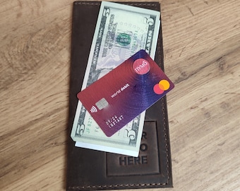 May include: A brown leather wallet with the words "RO HERE" embossed on the front. The wallet is open and contains two five dollar bills and a red and blue debit card with the words "world debit" printed on it.