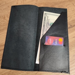 May include: Open black leather wallet with a five-dollar bill and a credit card visible. The wallet is open, revealing multiple compartments and a stitched edge. The credit card has the number 5885 visible.