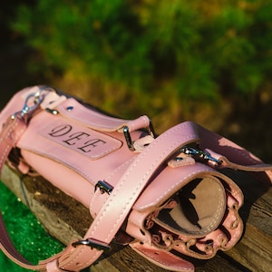 May include: A pink leather roll-up case with a strap and buckle closure. The case has the name "DEE" embossed on the front.